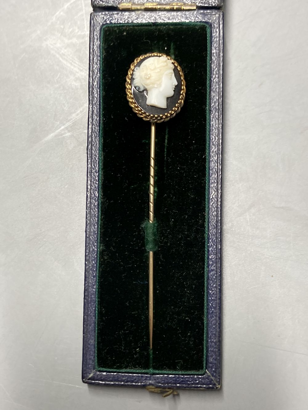 A cased early 20th century yellow metal and carved sardonyx set stick pin, 8cm and a similar shell stick pin, 56mm.